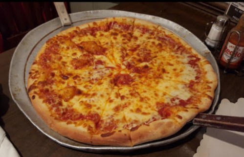 A large cheese pizza on a metal tray, with a golden crust and melted cheese, placed on a wooden table.
