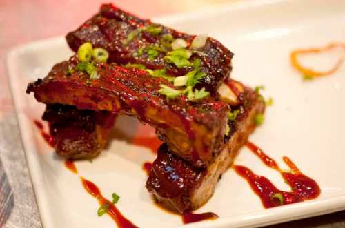 A plate of glazed barbecue ribs garnished with green onions and drizzled with sauce.