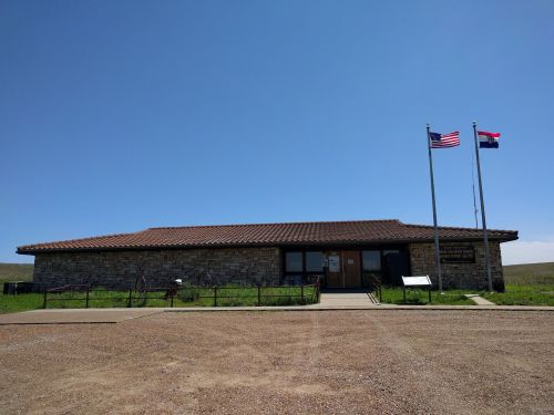 A stone building with a tiled roof, featuring American and state flags, set against a clear blue sky.