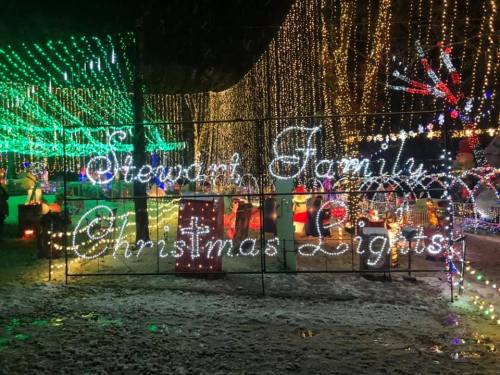 Colorful Christmas lights display with "Stewart Family Christmas Lights" sign, surrounded by festive decorations.
