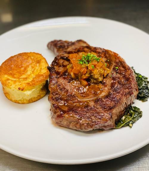 A beautifully cooked ribeye steak topped with a vegetable garnish, served with a fluffy soufflé on the side.