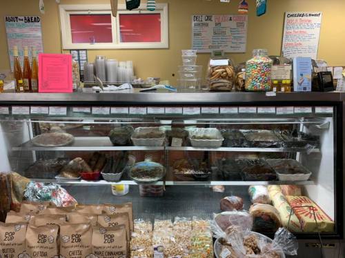 A display case filled with various baked goods and snacks, with shelves of jars and containers in the background.