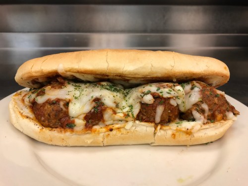 A meatball sub sandwich with melted cheese and herbs, served on a toasted hoagie roll.