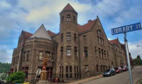 Historic stone building with a turret, located on Library Street, featuring a statue in front and a cloudy sky.