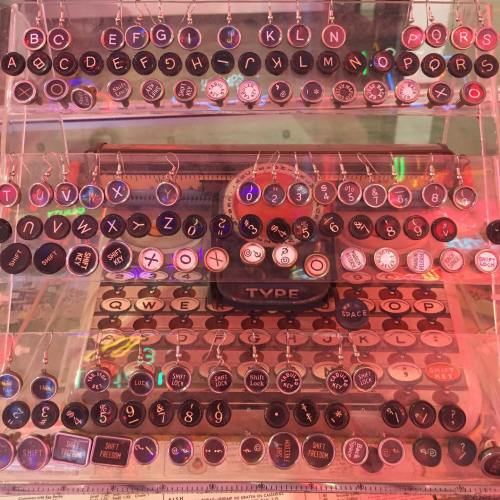 A display of colorful earrings shaped like letters and symbols, arranged in rows on a clear stand.