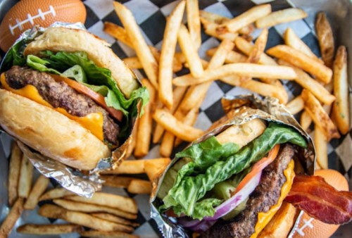 Two juicy burgers with lettuce, tomato, and cheese, served with a side of golden French fries on a checkered tray.