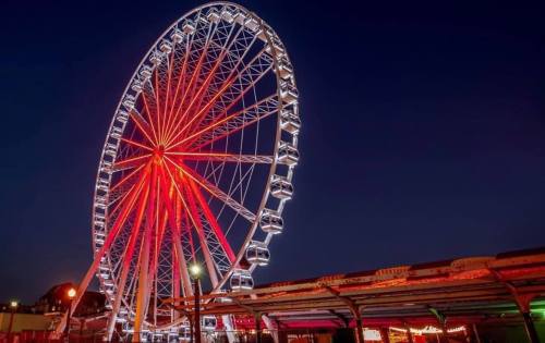 A brightly lit Ferris wheel at night, featuring red and white lights against a dark sky.