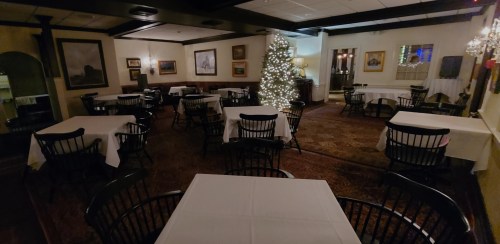 A cozy restaurant interior with empty tables, a decorated Christmas tree, and warm lighting.
