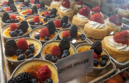 A display of creamy desserts, including crème brûlée topped with berries and mini cheesecakes with whipped cream.