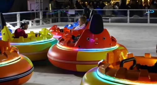 Colorful bumper cars with children inside, illuminated by neon lights, on a funfair ride.