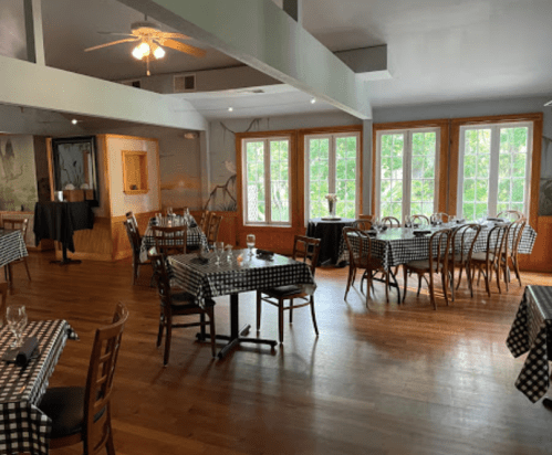 Interior of a restaurant with checkered tablecloths, wooden floors, and large windows letting in natural light.