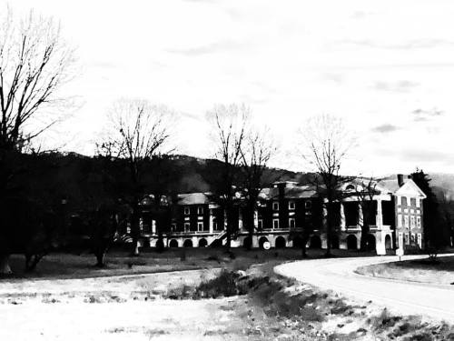 A black and white image of a large, old building surrounded by bare trees and a winding road.