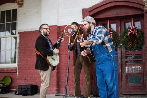 Three musicians perform outdoors, playing a banjo and guitar, with a vintage microphone and festive decorations in the background.