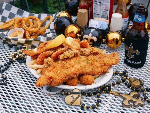A plate of fried fish, shrimp, and onion rings, served with lemon, fries, and a beer, surrounded by festive decorations.