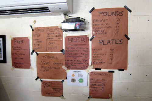 Menu board featuring prices for food items like brisket, ribs, and sides, along with drinks and merchandise.