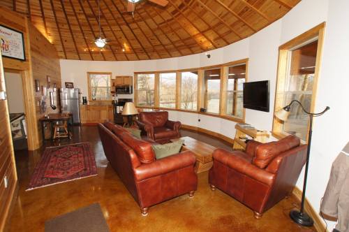 Cozy circular living room with leather sofas, wooden accents, large windows, and a rustic decor.