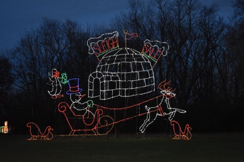 Colorful holiday lights depict a festive scene with a sleigh, snowman, and igloo against a twilight sky.