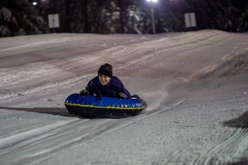A person joyfully sledding down a snowy hill on a blue inflatable tube at night.