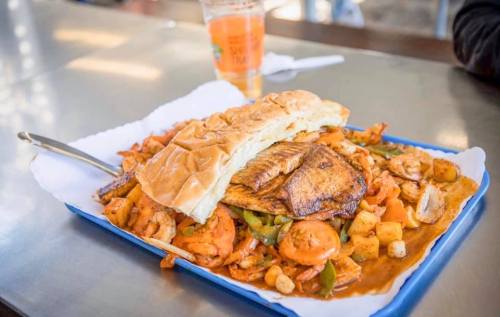 A large platter of grilled fish on a bed of mixed vegetables and fries, accompanied by a sandwich and a drink.