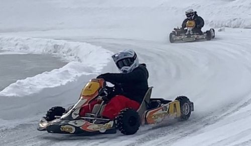 Two go-karts racing on a snowy track, with one driver leaning into a turn while the other follows closely behind.