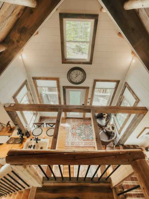 A cozy cabin interior viewed from above, featuring wooden beams, large windows, and a decorative rug.