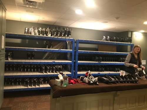 A woman prepares ice skates on a counter in a rental area with shelves of skates in the background.