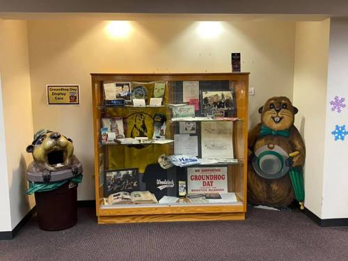 Display case featuring historical items and memorabilia, flanked by two groundhog mascots.