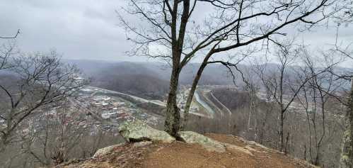 A view from a rocky overlook showing a valley, winding road, and distant mountains under a cloudy sky.