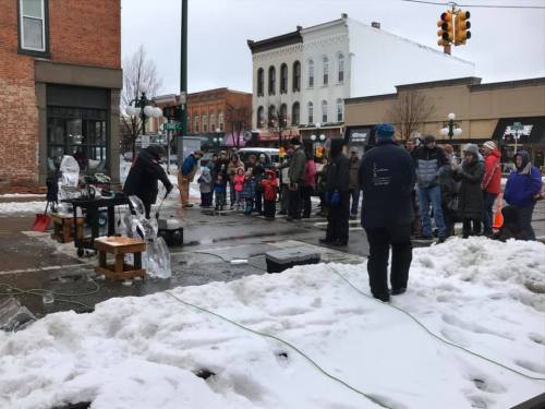 A crowd watches a street performance in winter, with snow on the ground and buildings in the background.