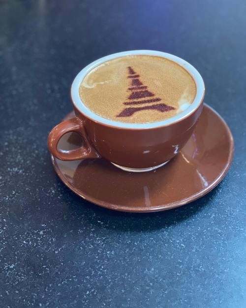A brown coffee cup on a saucer, filled with latte art resembling a tree design on top of the coffee.
