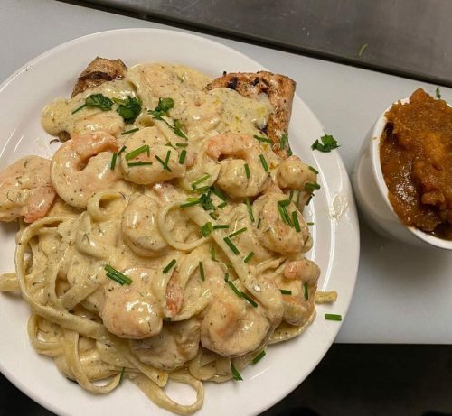 A plate of creamy shrimp fettuccine topped with chives, alongside a small bowl of pumpkin puree.