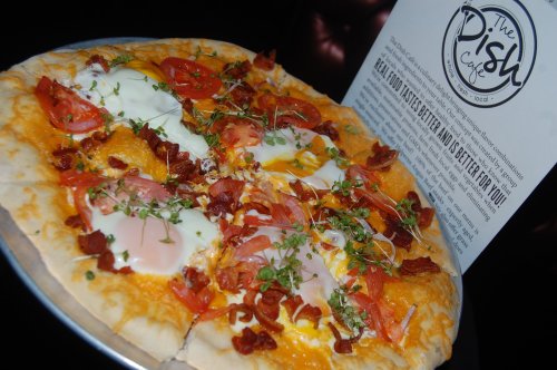 A delicious pizza topped with cheese, tomatoes, bacon, and eggs, served at The Dish Café.