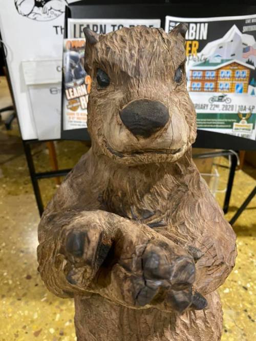 A carved wooden statue of a bear with a friendly expression, standing with its paws slightly raised.