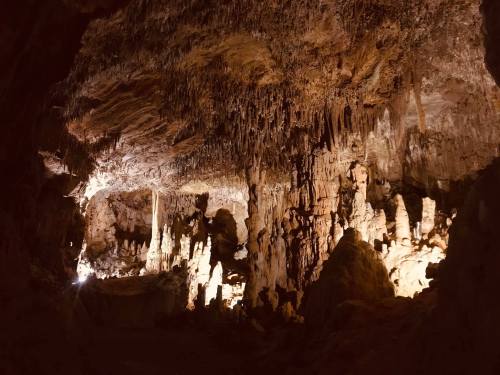 A dimly lit cave interior featuring stalactites and stalagmites, with illuminated rock formations creating a dramatic effect.