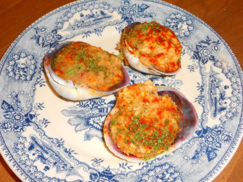 Three stuffed clams on a decorative blue and white plate, garnished with herbs and spices.