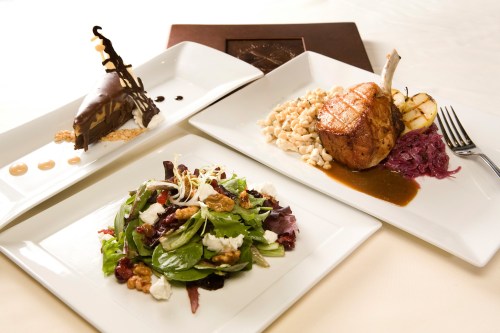 A gourmet meal featuring a salad, pork chop with sides, and a chocolate dessert on elegant white plates.