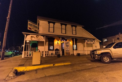 A two-story building at night with a sign for "Claud's Tavern" and a parked truck in front.
