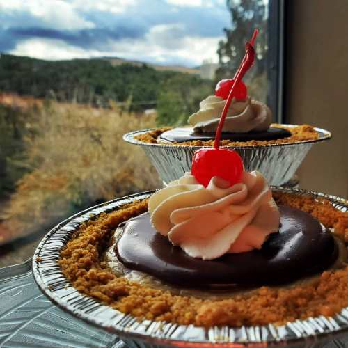 Two chocolate desserts with whipped cream and cherries, set against a scenic outdoor view.