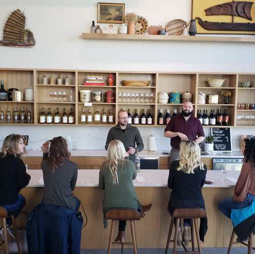 A group of people seated at a bar, engaging with two staff members behind a wooden counter in a cozy setting.