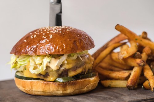 A juicy cheeseburger with lettuce and sauce, served on a sesame seed bun, alongside crispy French fries.