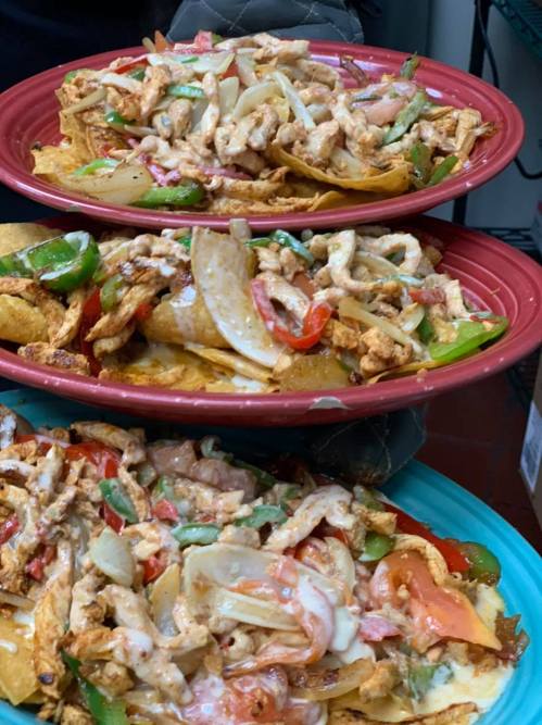 Three stacked plates of nachos topped with grilled chicken, bell peppers, onions, and a creamy sauce.