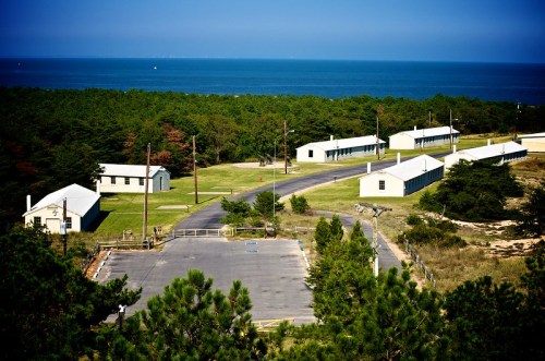 Aerial view of a coastal area with buildings, trees, and a clear blue ocean in the background.