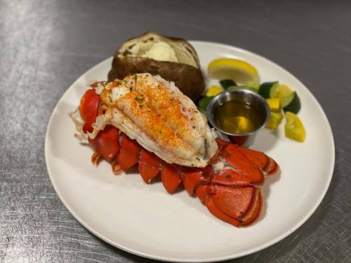 A plate featuring a lobster tail, baked potato, lemon wedges, and a small bowl of melted butter.