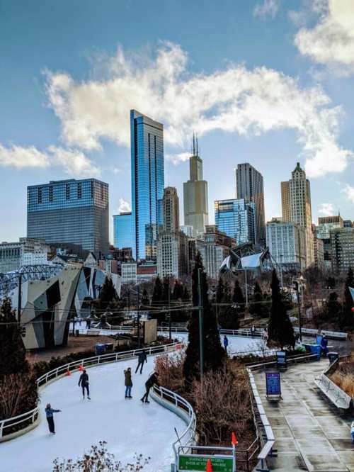 A city skyline with tall buildings, including a skyscraper, and an outdoor ice skating rink in the foreground.