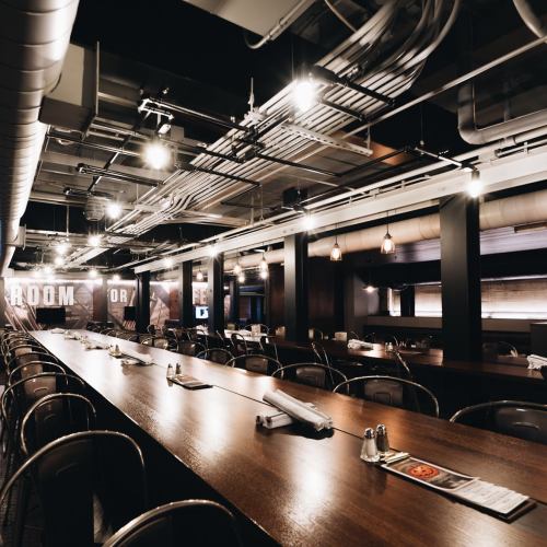 A modern restaurant interior featuring a long wooden table, industrial lighting, and a sleek, minimalist design.