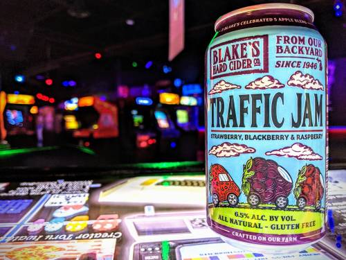 A can of Blake's Hard Cider "Traffic Jam" featuring strawberries, blackberries, and raspberries, set against arcade games.