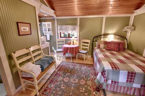 Cozy bedroom with a bed, small dining table, and rustic decor in warm green tones and wooden accents.