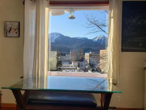 A clear view from a window showing mountains and a cityscape, with a glass table in the foreground.