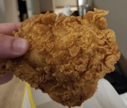 A hand holding a large, crispy fried chicken piece with a golden-brown coating.