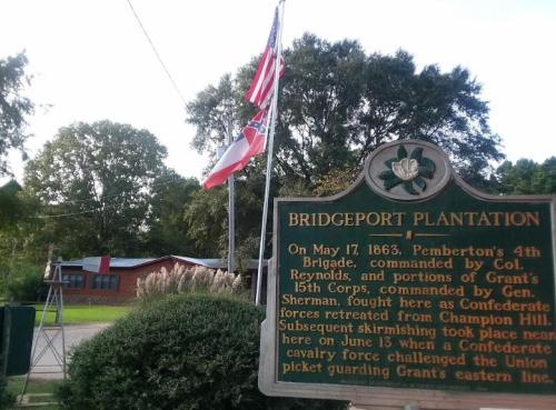 Historical marker at Bridgeport Plantation with flags, detailing a Civil War skirmish on May 17, 1863.